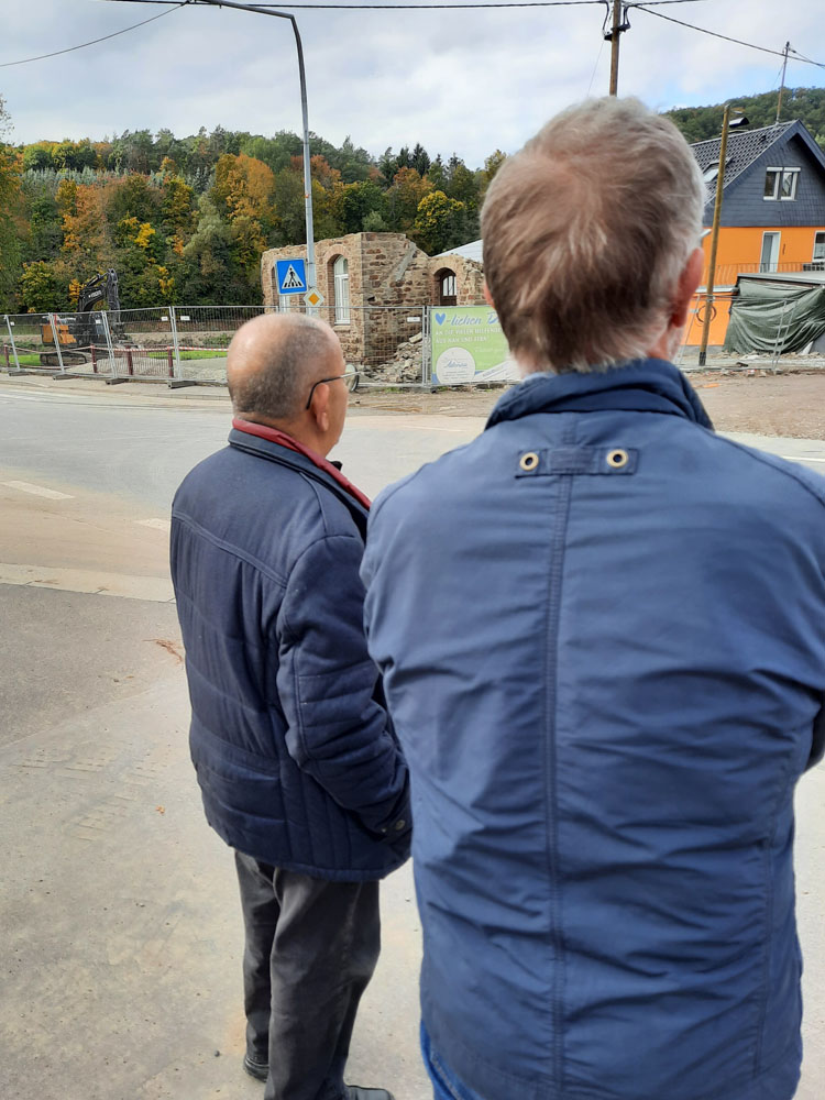 Das Bild zeigt Pfr. Schäfer vor dem zerstörten Dorfgemeinschaftshaus in der Gemeinde Müsch. Dort soll jetzt eine Gedenkstätte entsttehen.